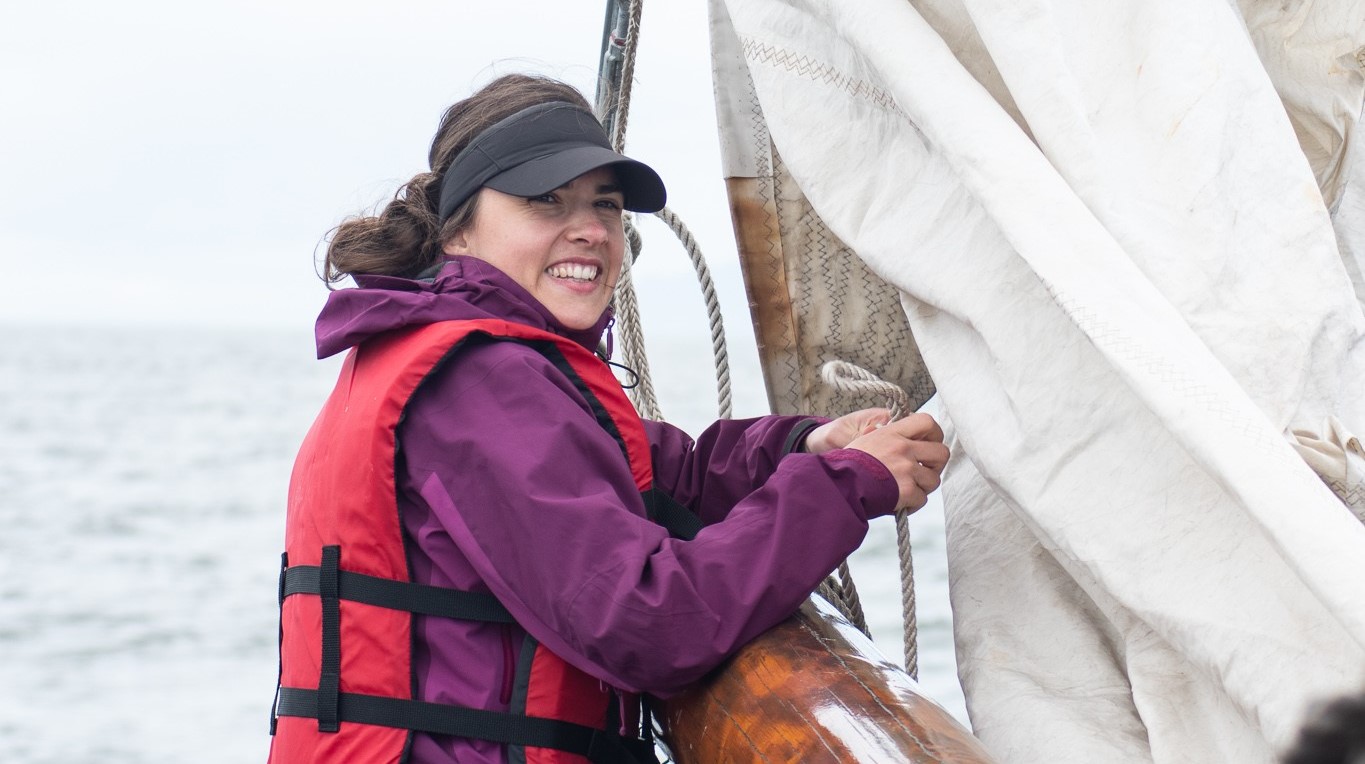 Yasmin Schepens tying knot in rope, sitting on sailboat during Ocean Bridge program.